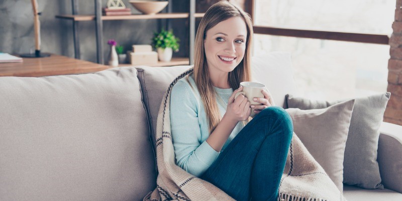 Women drinking coffee on couch wrapped in a blanket
